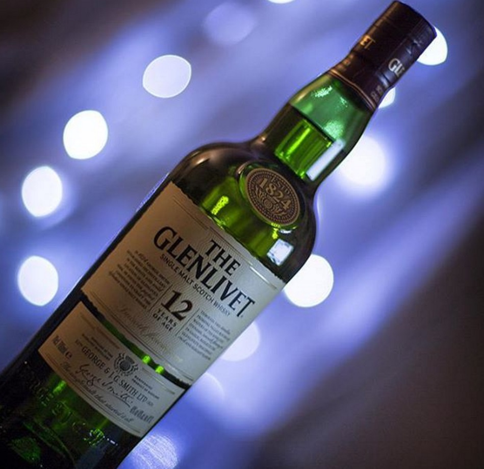A bottle of Glenlivet whisky (green with cream label) and a blue tinted background with fairy lights out of focus (bokeh)